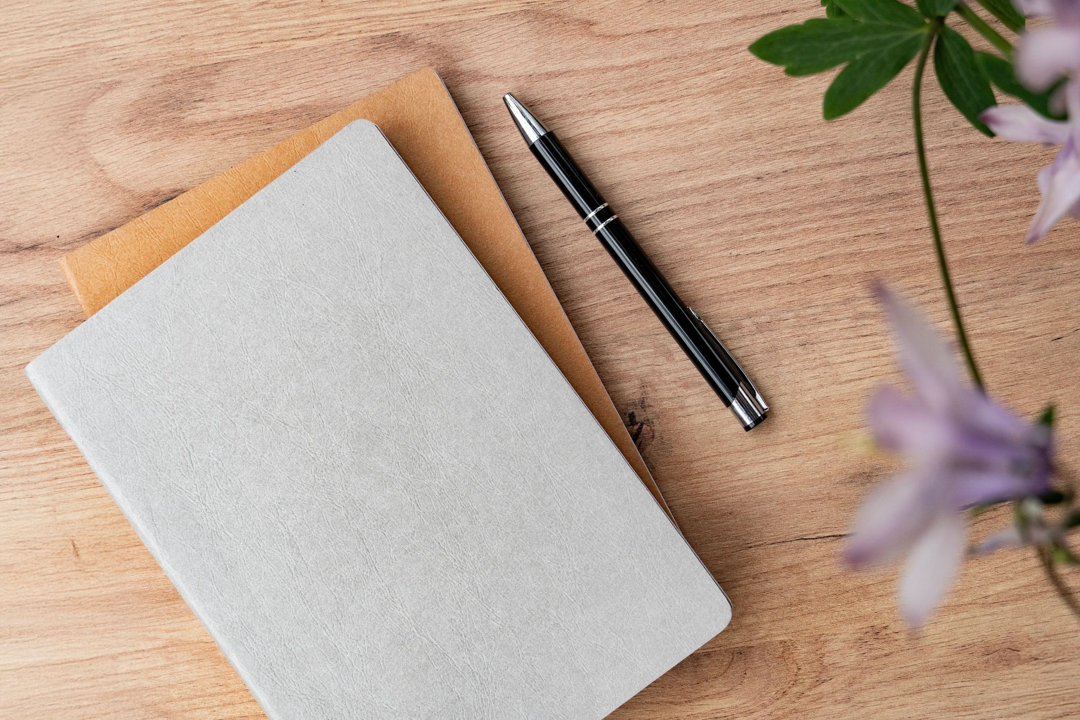 Notebook and pen styled with flowers on a wooden surface