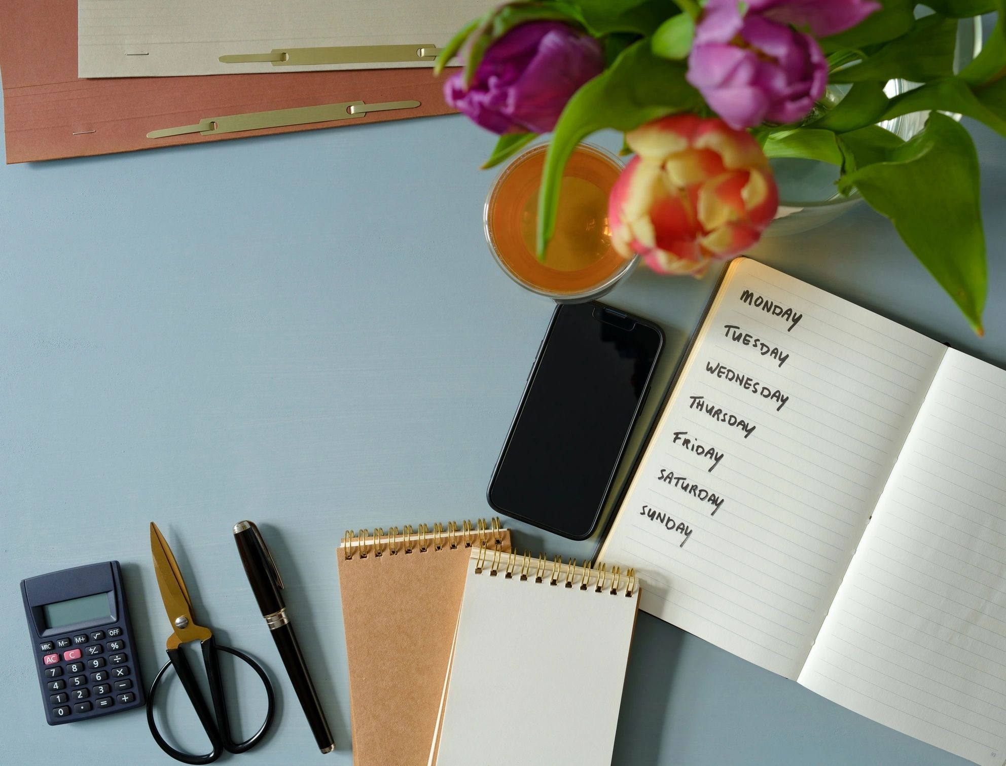Notebook, tea, smartphone, and stationery arranged on a clean workspace